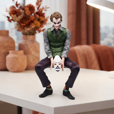 A small Joker sitting action figure displayed on a minimalist desk with warm terracotta and burnt sienna decor elements.